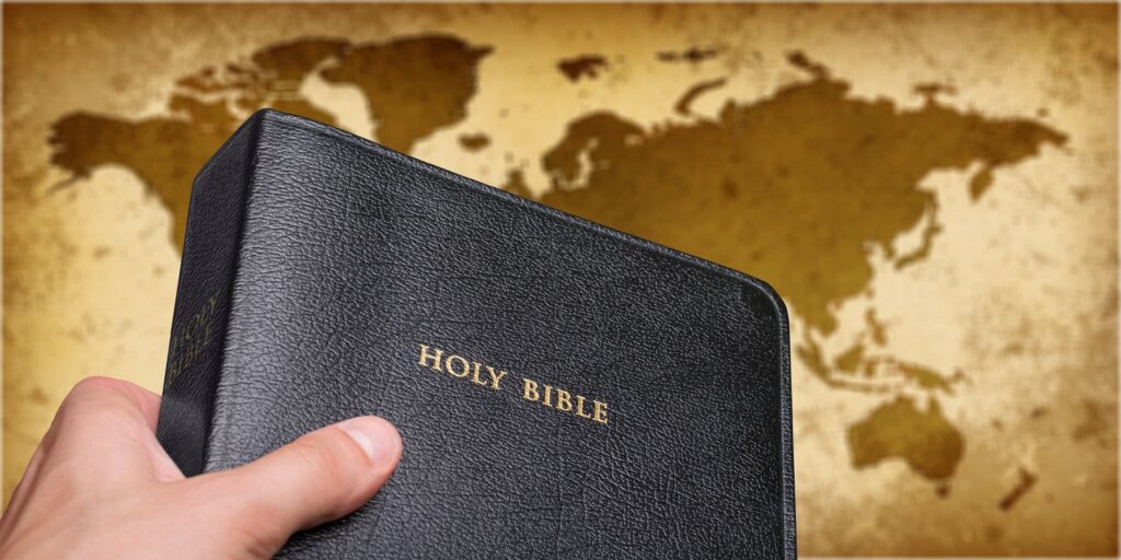 Image of hand holding Bible over world map