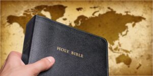 Image of hand holding Bible over world map