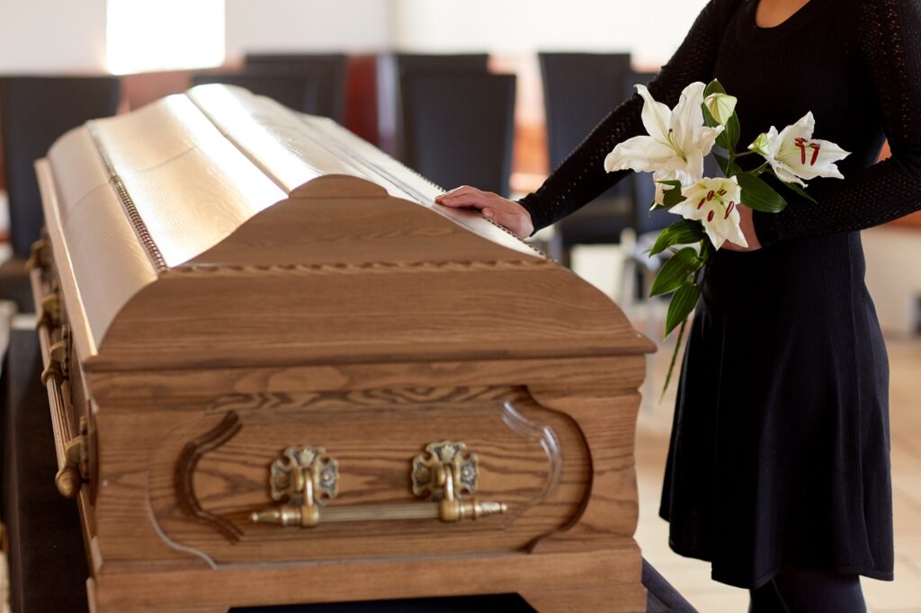 Image of woman holding flowers and touching a casket