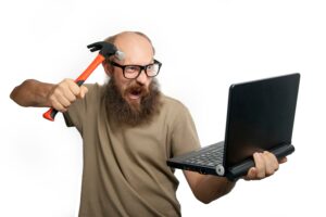 Photo of a man about to smash his laptop with a hammer.